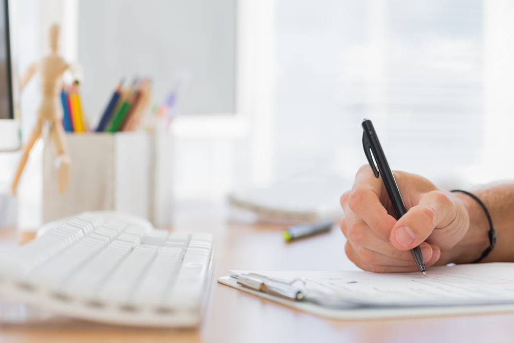 Close up of a hand writing in a modern office on a clipboard